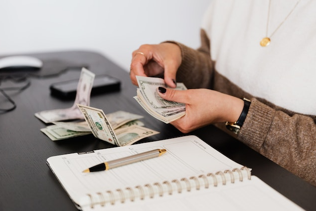 Person counting dollar bills at a desk with a notebook, symbolizing passive income ideas and online earning opportunities.